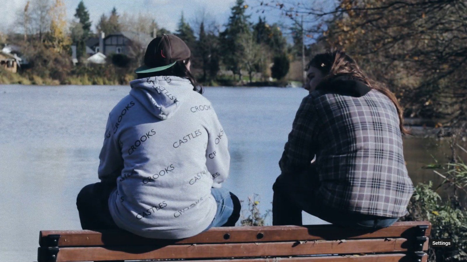 The two teens sitting together on a bench by a lake