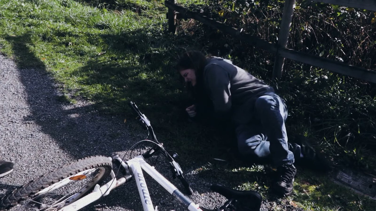 A teen crouched on the ground next to a fallen bicycle after a fall while learning to ride